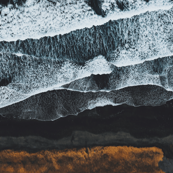Events Guys An aerial view of a sandy beach with waves crashing onto the shore.