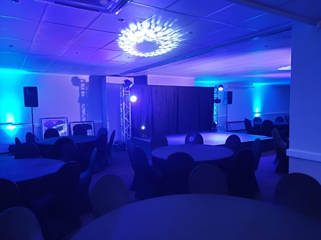 Events Guys An event space with blue lighting, equipped with tables and chairs for guests.