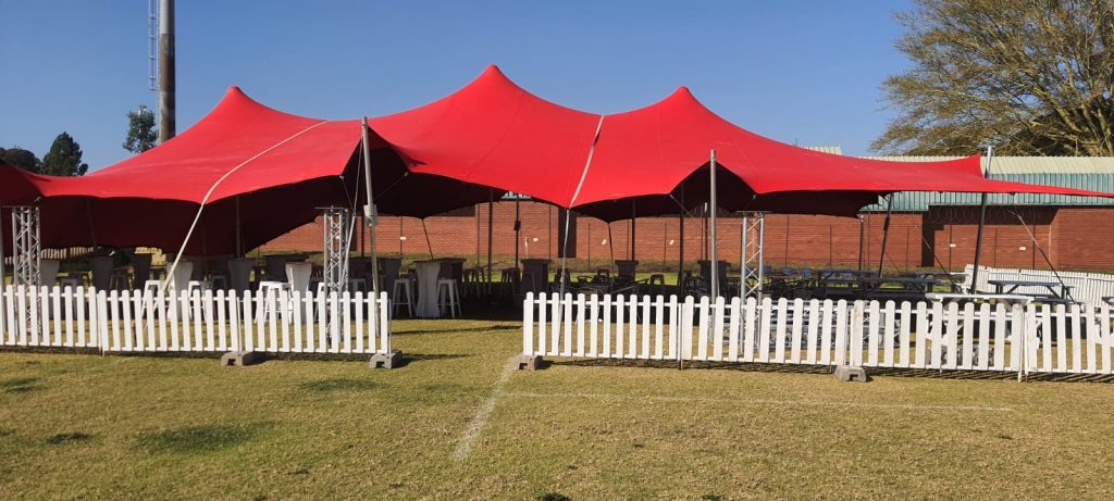 Events Guys An impressive red tent erected in a serene grassy area, perfect for hosting events.