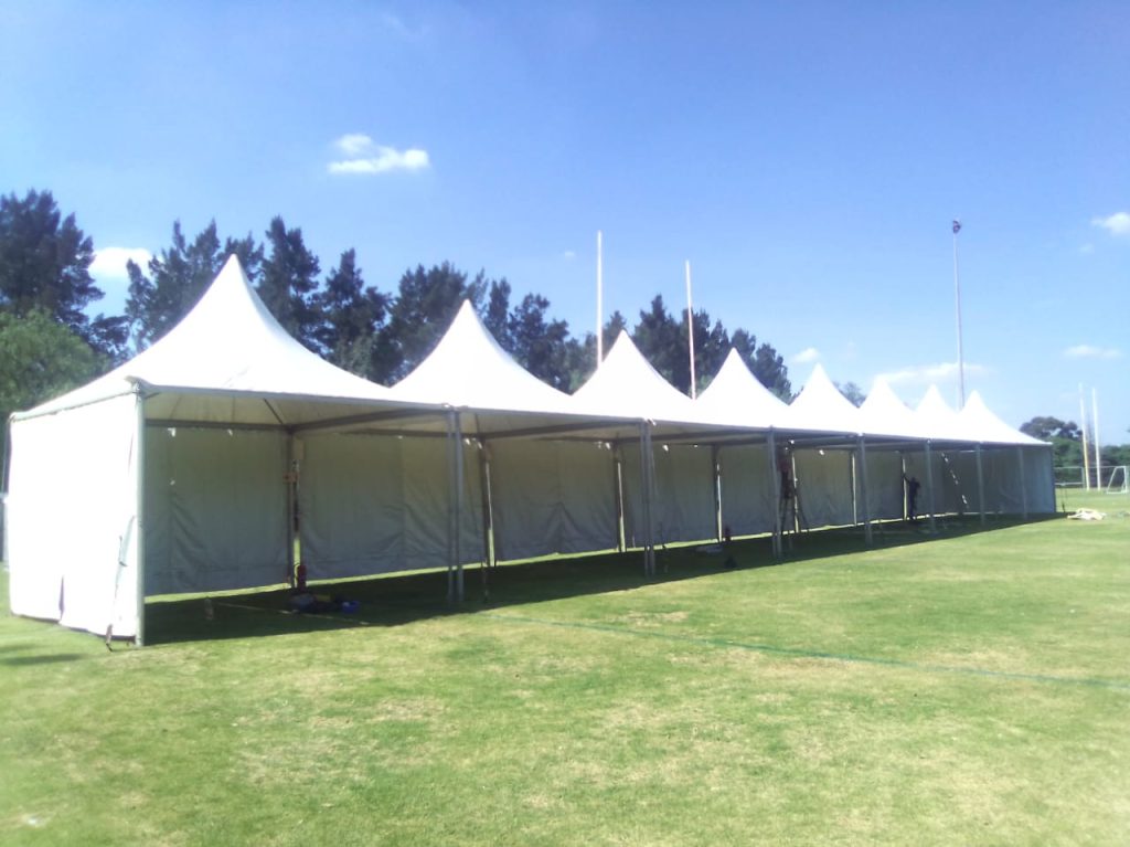 Events Guys Stretch tents for hire dot the green grass, their white peaks perfectly contrasting against a brilliant blue sky.