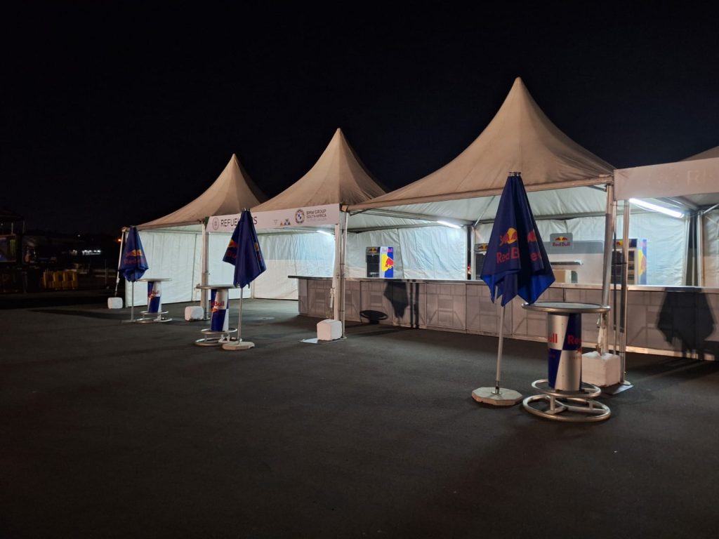 Reliable and Affordable Tents for Rent in Sunny South Africa 2 Events Guys Three white tents for rent with tables and branded umbrellas are set up outdoors at night.